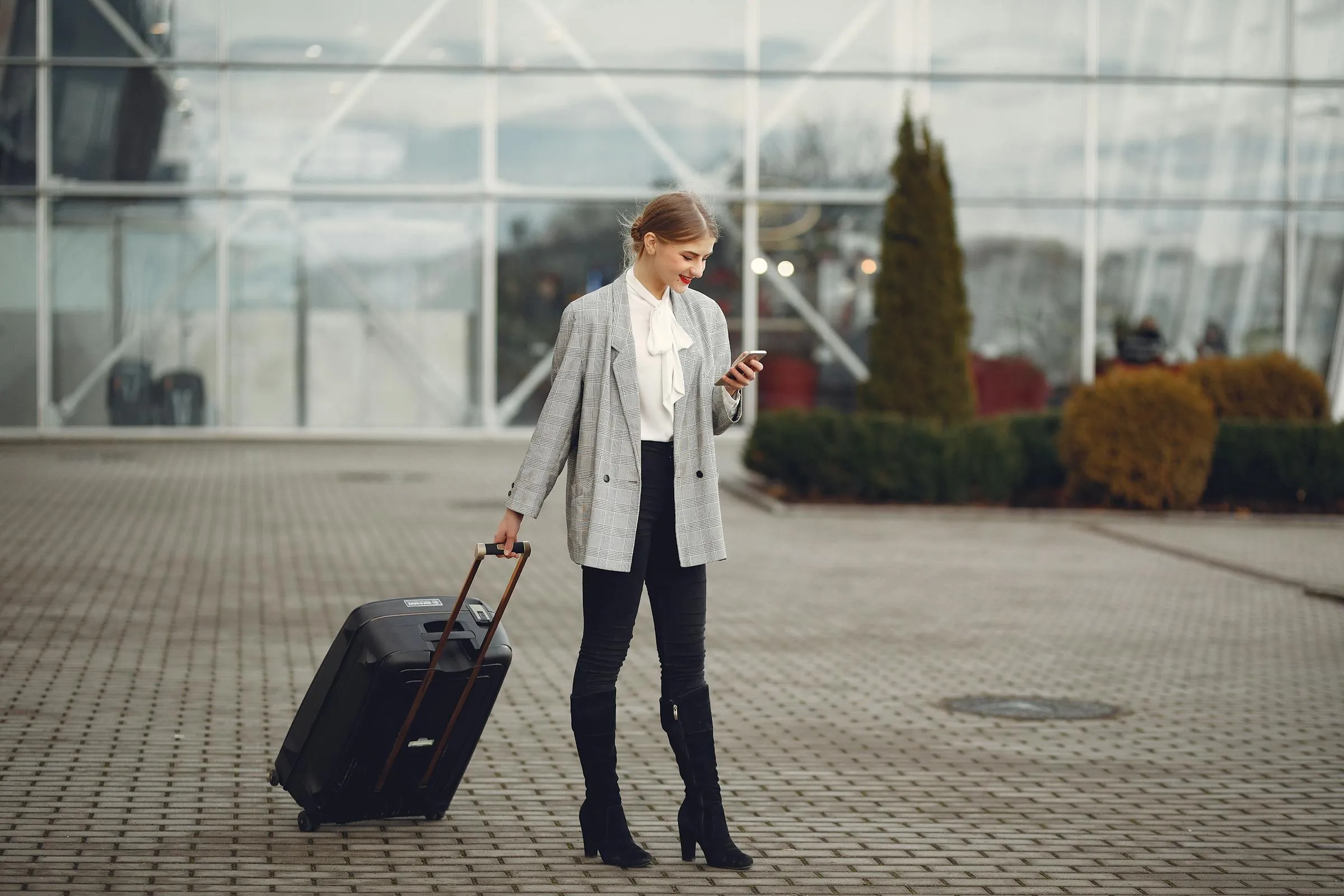 Traveler using her smartphone outside an airport terminal with luggage